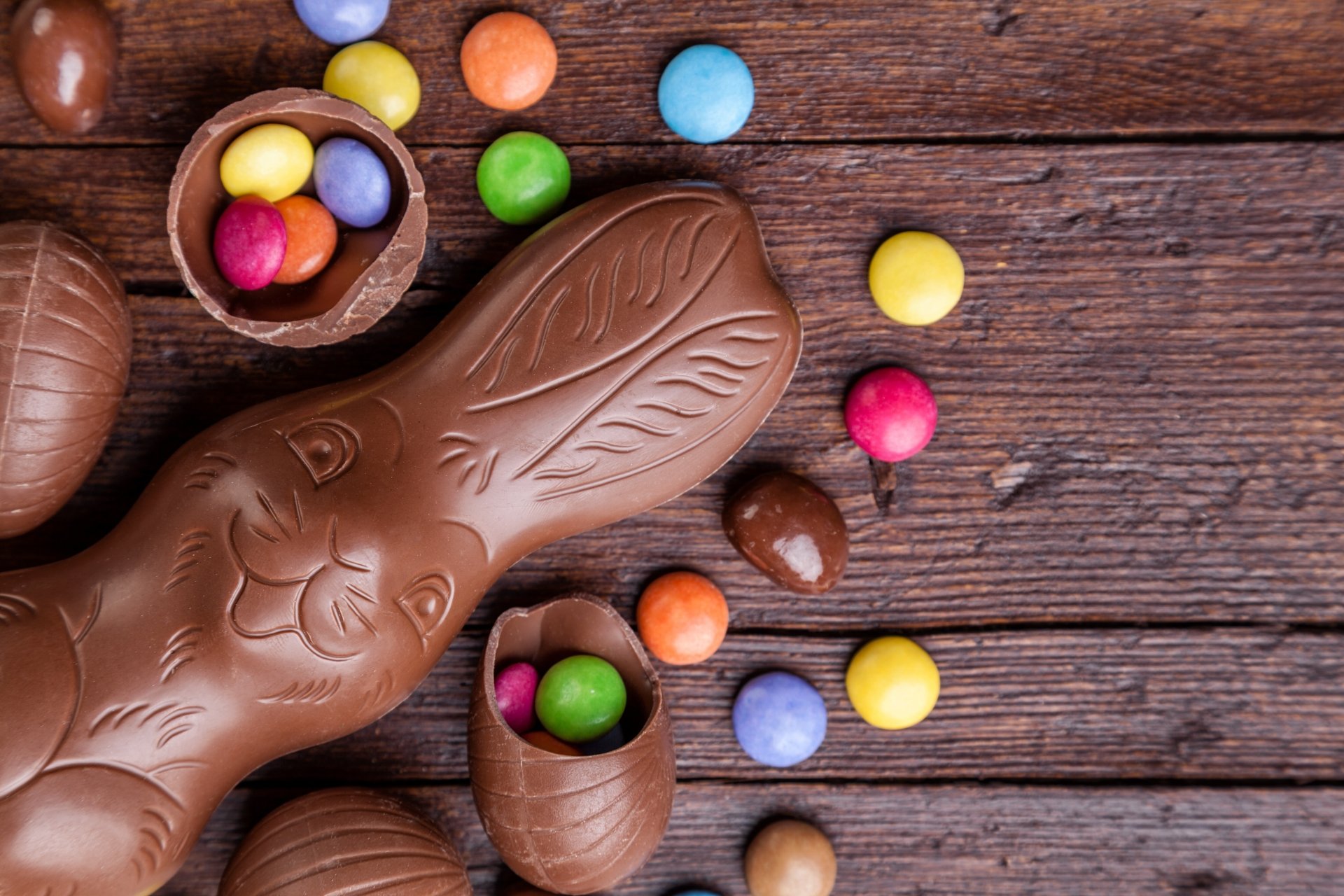 4K Ultra HD desktop wallpaper featuring colorful Easter candy and chocolate, including a large chocolate bunny and scattered candy pieces on a rustic wooden surface.