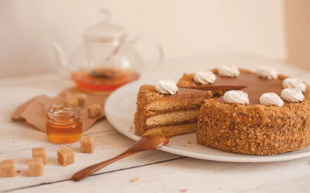 HD desktop wallpaper showcasing a honey-glazed layered cake with whipped cream, surrounded by sugar cubes, honey jar, and a glass teapot in a still life dessert setting.