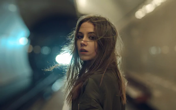 HD desktop wallpaper featuring Ksenia Kokoreva, a brunette woman with long hair and brown eyes, standing in a softly lit tunnel background.