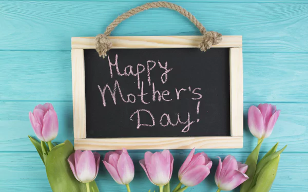 Pink tulip flowers surround a small chalkboard with Happy Mother's Day! written, set against a blue wooden background in a 4K Ultra HD holiday-themed wallpaper.