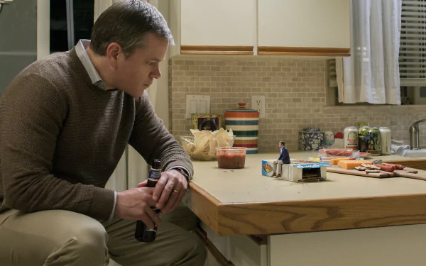 HD desktop wallpaper from Downsizing featuring Matt Damon observing a tiny figure next to regular-sized household items.