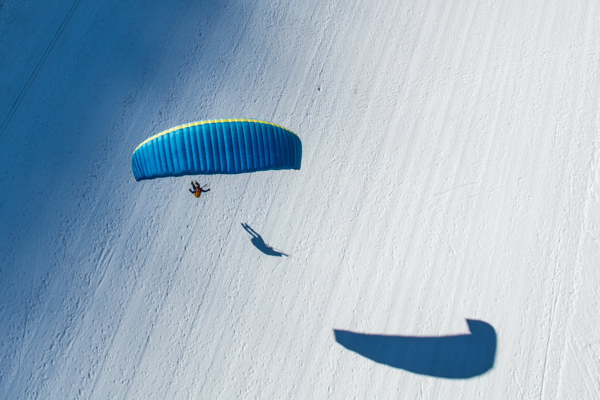 HD desktop wallpaper showing a solo paraglider soaring above a snowy landscape, capturing the thrill and freedom of the sport in vivid detail.