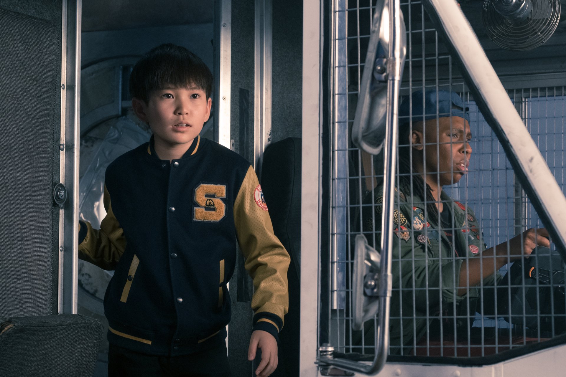 5K Ultra HD desktop wallpaper: a Ready Player One movie still showing two young actors in a metal booth — one in a varsity jacket, the other at the wheel, tense and alert.