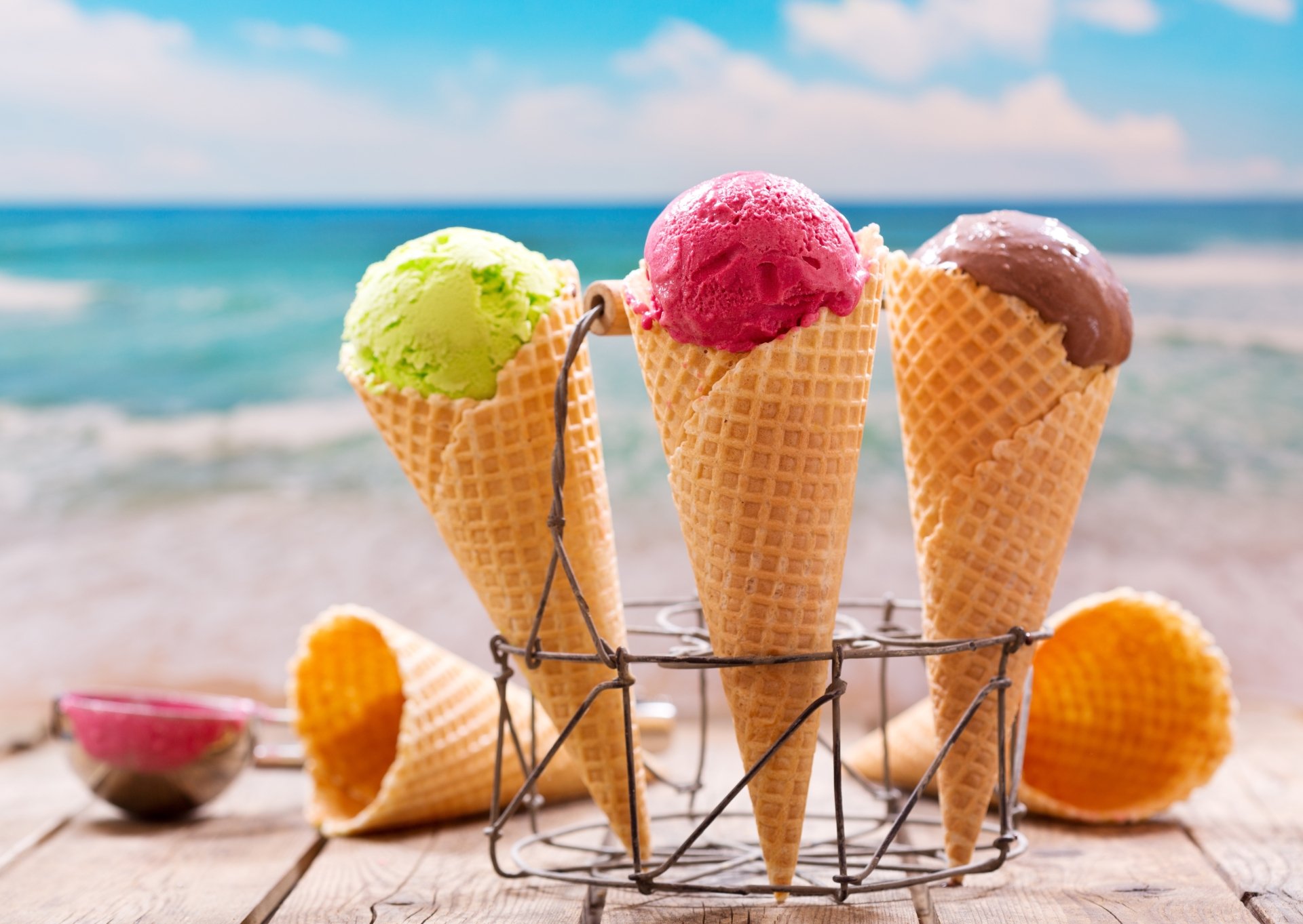 A 4K Ultra HD close-up of three colorful ice cream scoops in waffle cones with a blurred ocean background, showcasing food and depth of field on a PC desktop wallpaper.