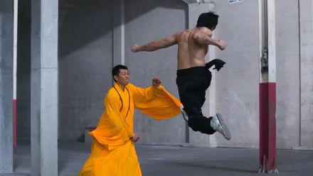 4K Ultra HD PC desktop wallpaper from the movie Birth of the Dragon — shirtless fighter midair kick toward an opponent in a flowing yellow robe inside a concrete warehouse.