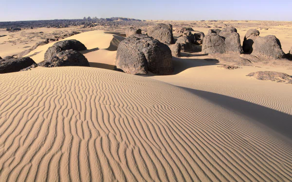 HD desktop wallpaper featuring the rippled sand dunes and rocky formations of Tassili N'Ajjer desert in Algeria, showcasing Africa's natural desert landscape.
