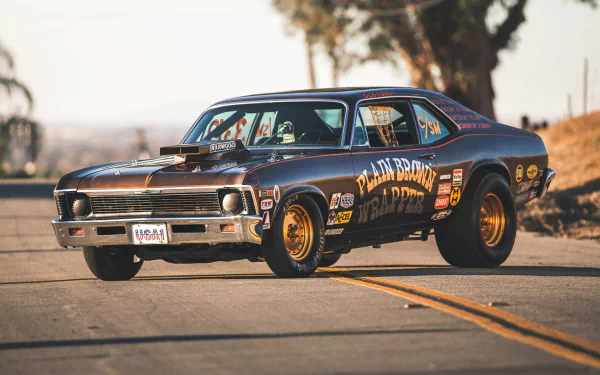 Chevrolet Nova SS race vehicle with sponsor decals on a sunlit road, shallow depth of field; HD PC desktop wallpaper background.