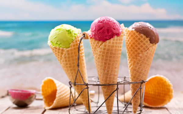 A 4K Ultra HD close-up of three colorful ice cream scoops in waffle cones with a blurred ocean background, showcasing food and depth of field on a PC desktop wallpaper.