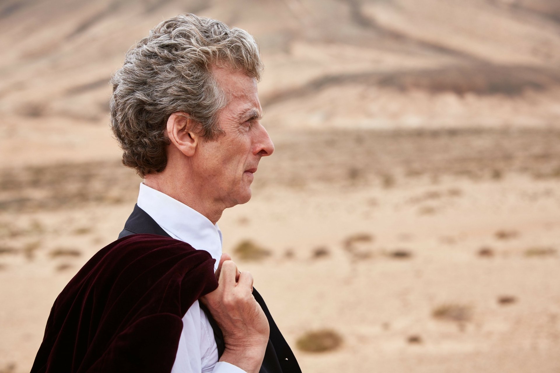 4K Ultra HD PC desktop wallpaper: side profile of the 12th Doctor (Doctor Who, 2005) standing in a windswept desert, cloak draped over his shoulder.