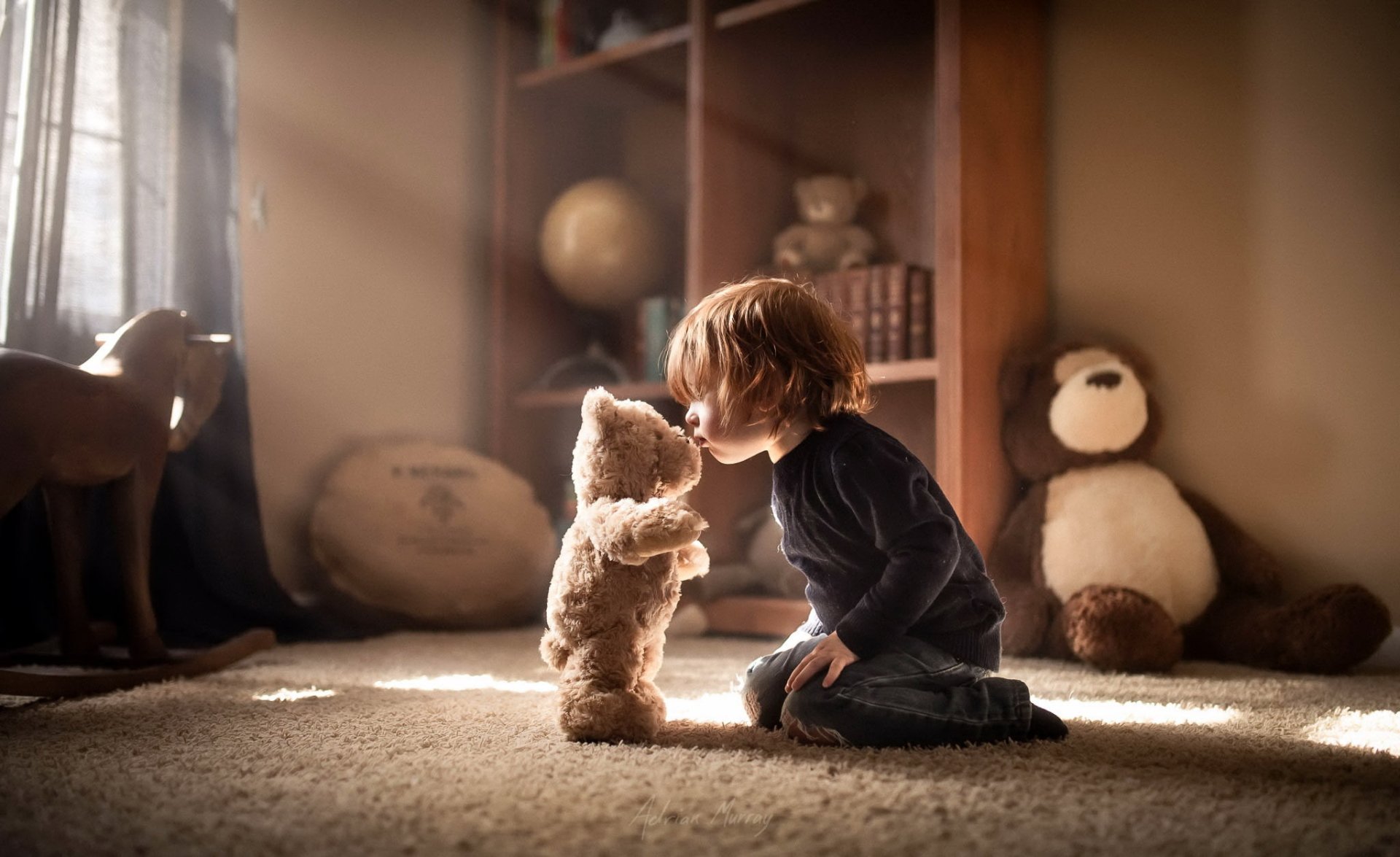 A little boy sits on the floor in a sunbeam, holding and facing a stuffed teddy bear in a softly lit room, captured in HD photography for a PC desktop wallpaper.