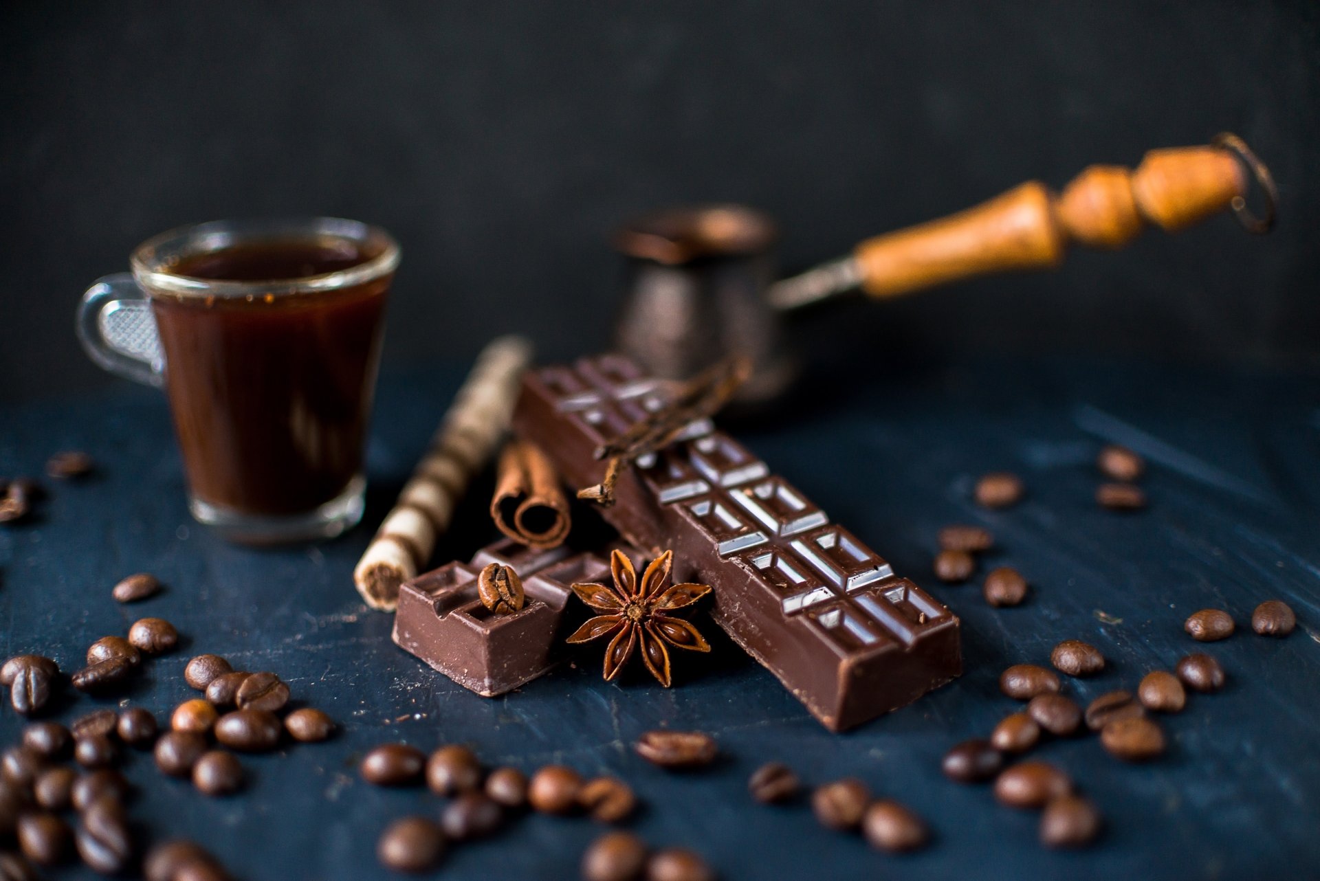 HD still life desktop wallpaper featuring cinnamon sticks, star anise, coffee beans, and rich chocolate pieces with a small cup of coffee in the background.