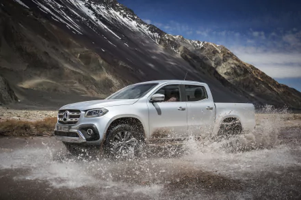 Silver Mercedes‑Benz X‑Class pickup vehicle splashes through a mountain stream against rugged peaks; 4K Ultra HD PC desktop wallpaper background.