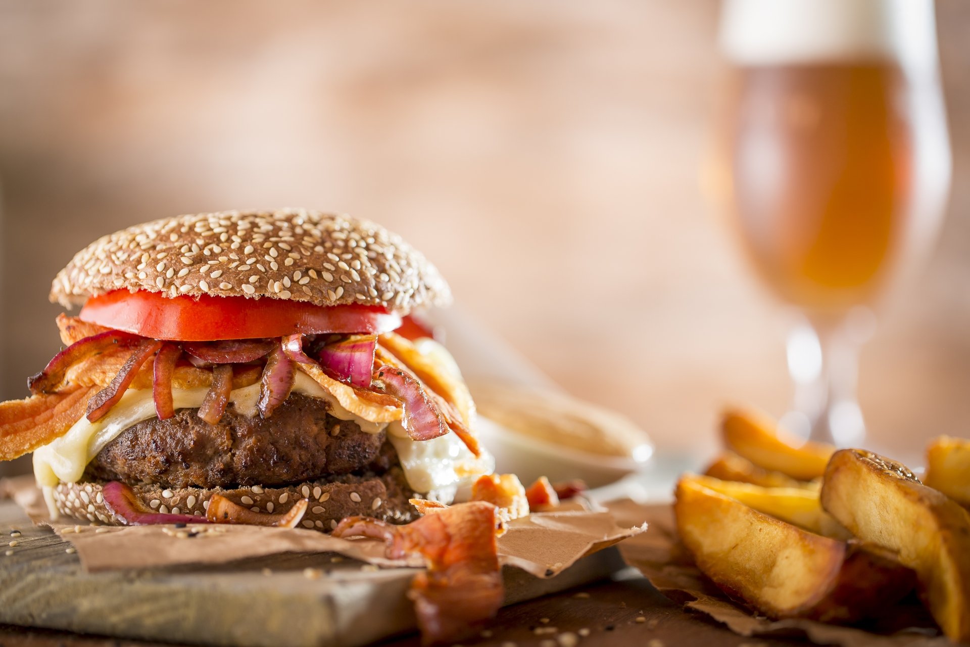 4K Ultra HD PC desktop wallpaper featuring a juicy bacon cheeseburger with tomato, lettuce, and fries, accompanied by a blurred glass of beer in the background.