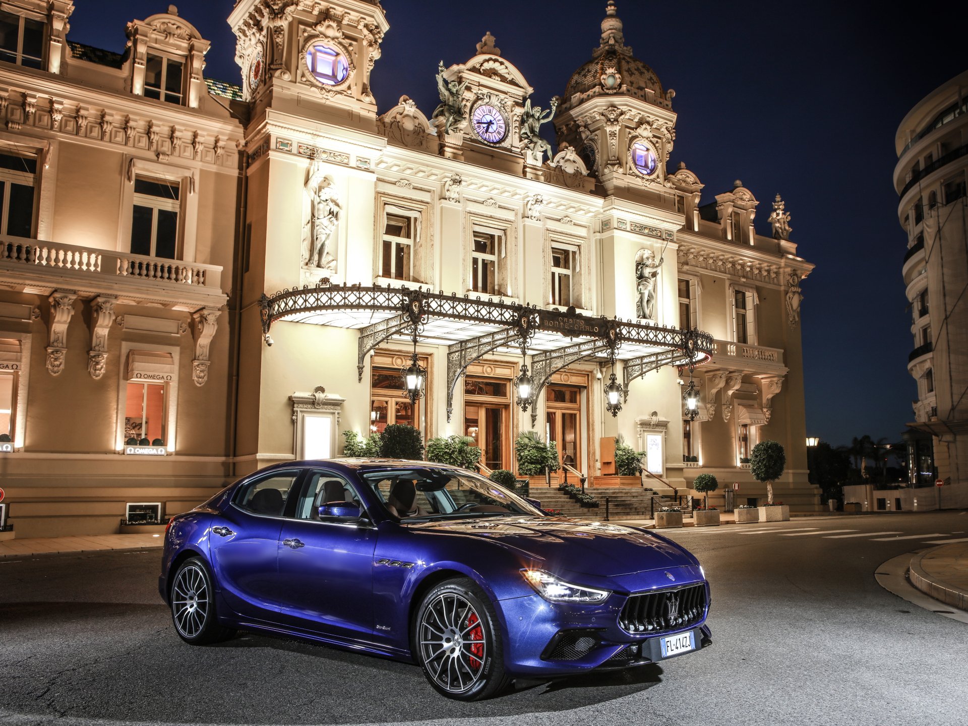 Blue Maserati Ghibli sedan parked before an illuminated historic casino at night, 4K Ultra HD PC desktop wallpaper of a luxury car/vehicle.