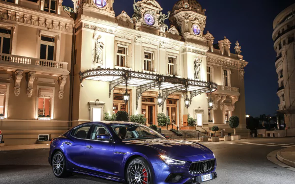 Blue Maserati Ghibli sedan parked before an illuminated historic casino at night, 4K Ultra HD PC desktop wallpaper of a luxury car/vehicle.