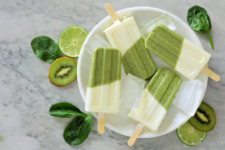 A 4K Ultra HD still life of kiwi and cream popsicles on a white plate, surrounded by fresh kiwi slices, lime halves, and spinach leaves on a marble surface.