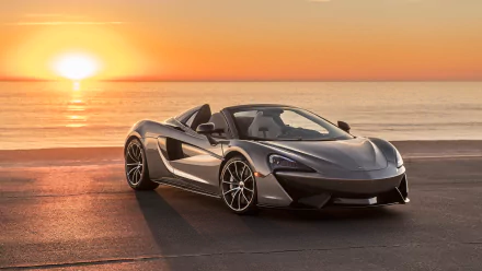 A silver McLaren 570S Spider supercar parked by the ocean at sunset. HD desktop wallpaper background.