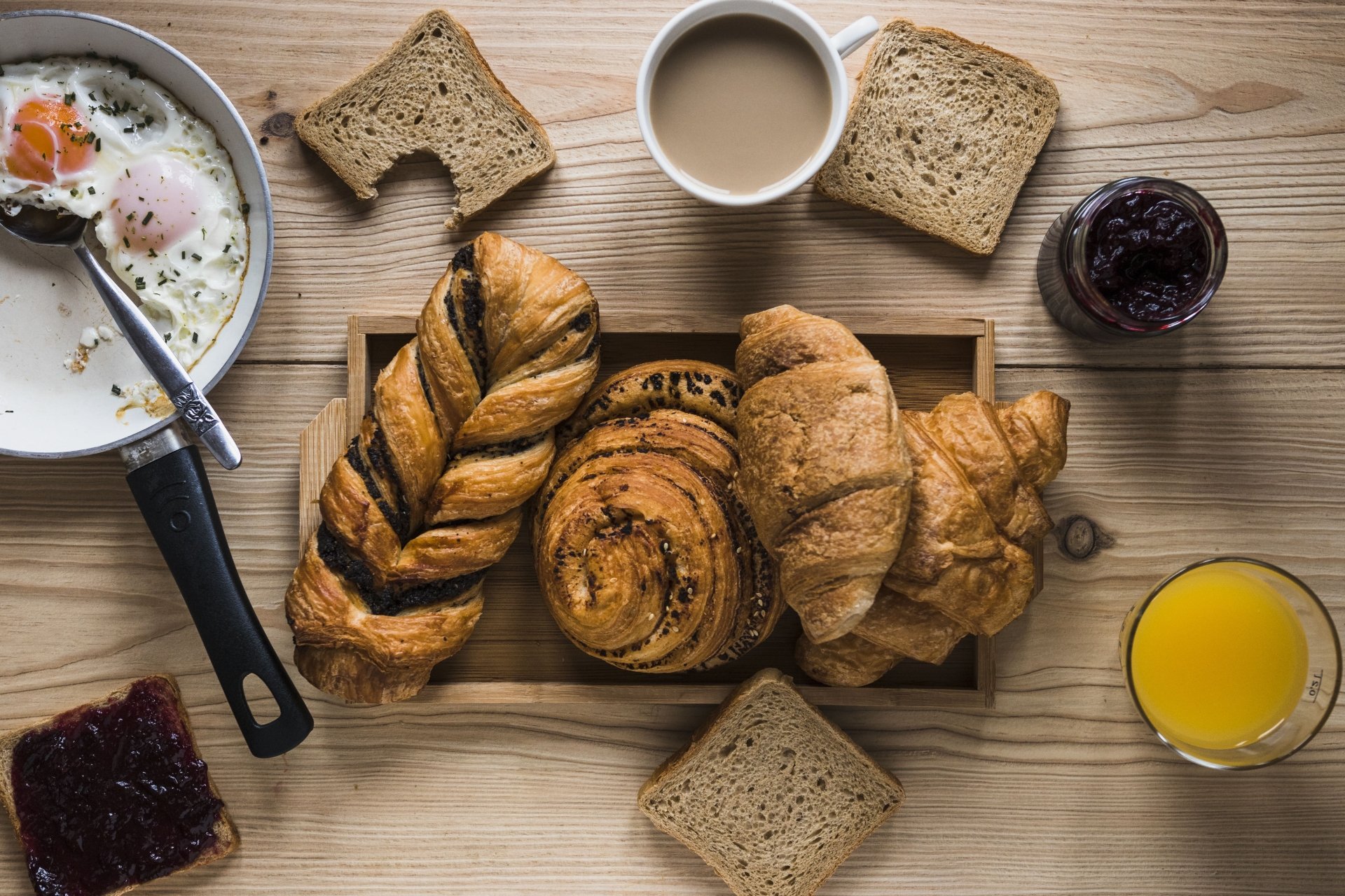 5K Ultra HD PC wallpaper still life of breakfast viennoiserie: croissants, braided and cinnamon rolls on a tray, toast, coffee, orange juice and jam on a wooden table.