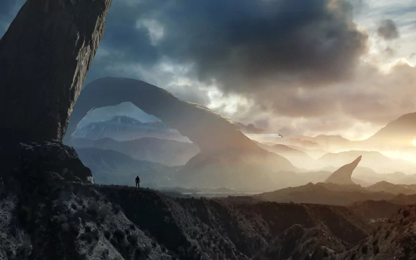 HD desktop wallpaper featuring a stunning sci-fi mountain landscape with dramatic rock formations and a lone figure standing on a ridge under a moody, cloud-filled sky.
