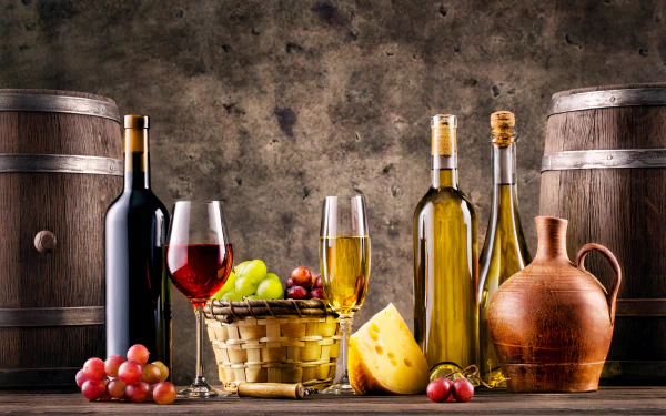 5K Ultra HD PC desktop wallpaper still life: wine bottles and glasses, oil jug, basket of grapes and cheese arranged between wooden barrels.
