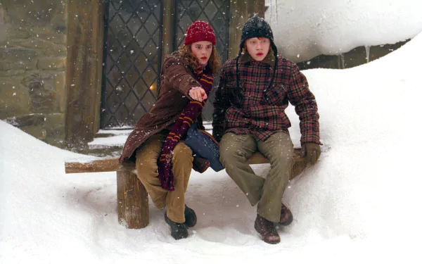 HD desktop wallpaper: Ron Weasley and Hermione Granger bundled in winter coats, sitting on a snowy bench in a scene from Harry Potter and the Prisoner of Azkaban.
