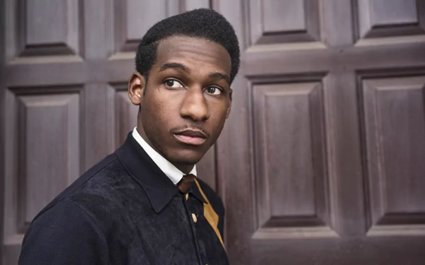 HD desktop wallpaper featuring a portrait of a man dressed in a smart outfit posing in front of a wooden panel door, tagged Leon Bridges.
