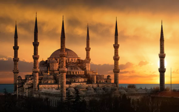 8K Ultra HD wallpaper of the Sultan Ahmed Mosque at sunset, showcasing its majestic domes and minarets against a vibrant, glowing sky.