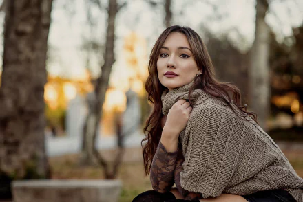 HD desktop wallpaper of a brunette model woman with long hair, brown eyes and lipstick, posed outdoors with shallow depth of field, wearing a textured knit shawl.