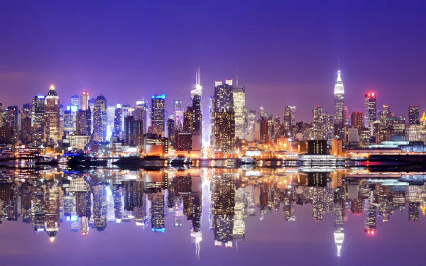HD desktop wallpaper of New York City at night, featuring illuminated skyscrapers and their reflections on water, capturing the vibrant cityscape of the USA.