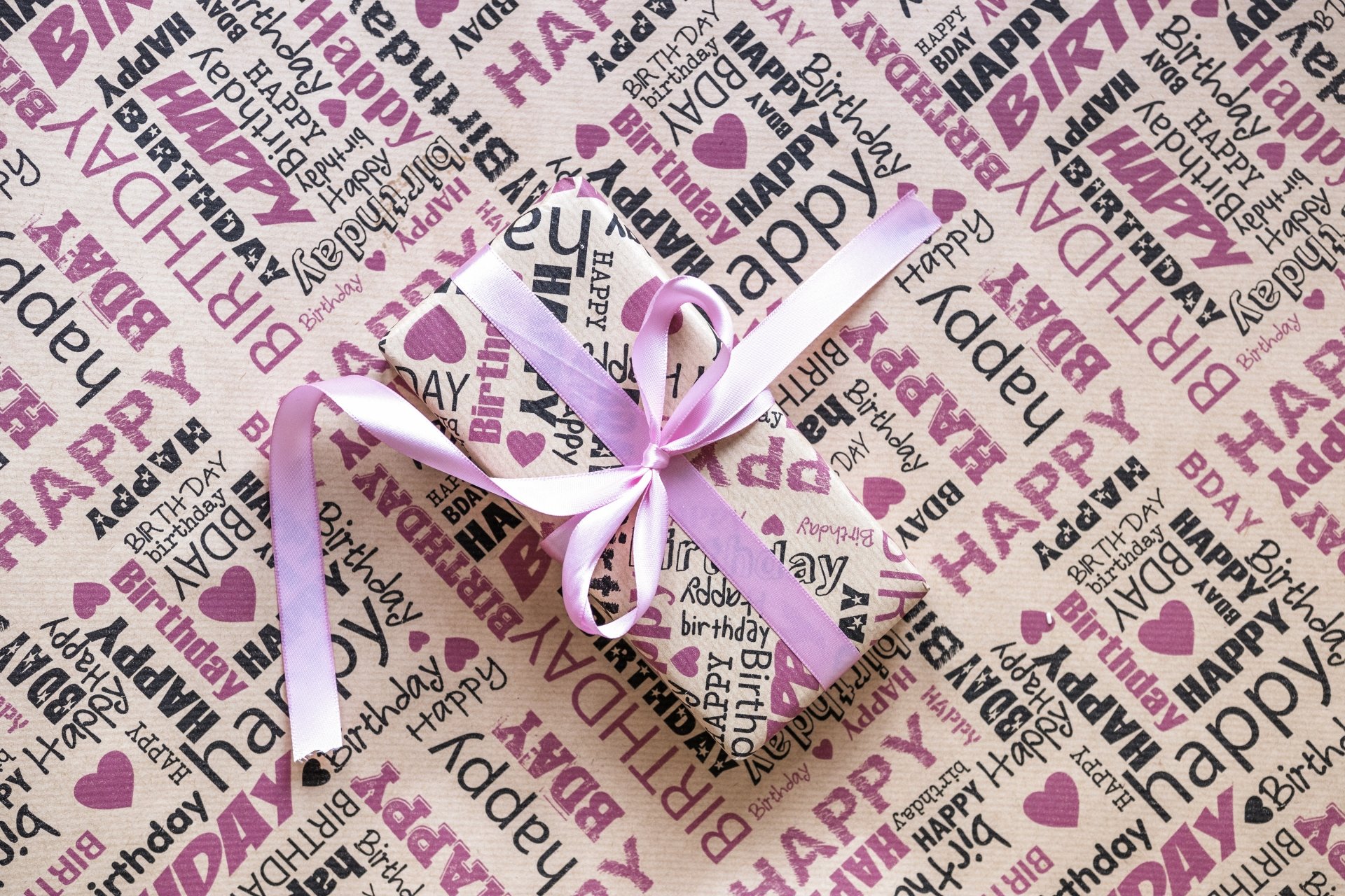 A 4K Ultra HD desktop wallpaper featuring a wrapped birthday gift with a pink ribbon on a background covered in colorful Happy Birthday text.