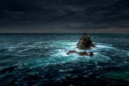 HD desktop wallpaper featuring a dramatic ocean scene with a rocky outcrop under a stormy sky, capturing the powerful beauty of nature and the horizon in the distance.