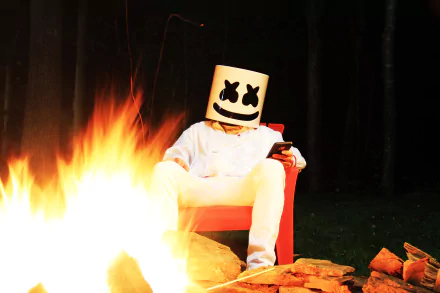 Marshmello, the DJ, sits in a chair beside a campfire in this HD desktop wallpaper and background.