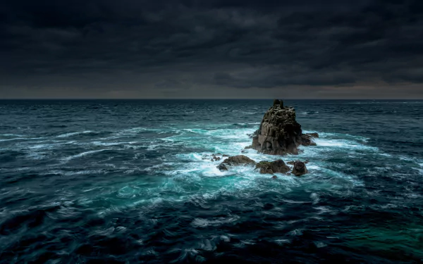 HD desktop wallpaper featuring a dramatic ocean scene with a rocky outcrop under a stormy sky, capturing the powerful beauty of nature and the horizon in the distance.