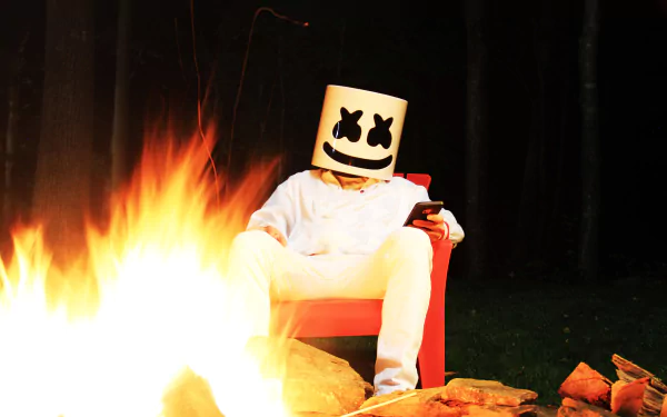 Marshmello, the DJ, sits in a chair beside a campfire in this HD desktop wallpaper and background.