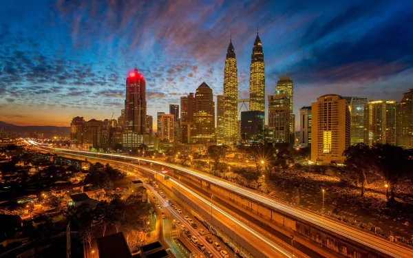 Nighttime cityscape of Kuala Lumpur featuring illuminated Petronas Towers, skyscrapers, and busy roads under a vibrant, colorful sky in this HD desktop wallpaper.