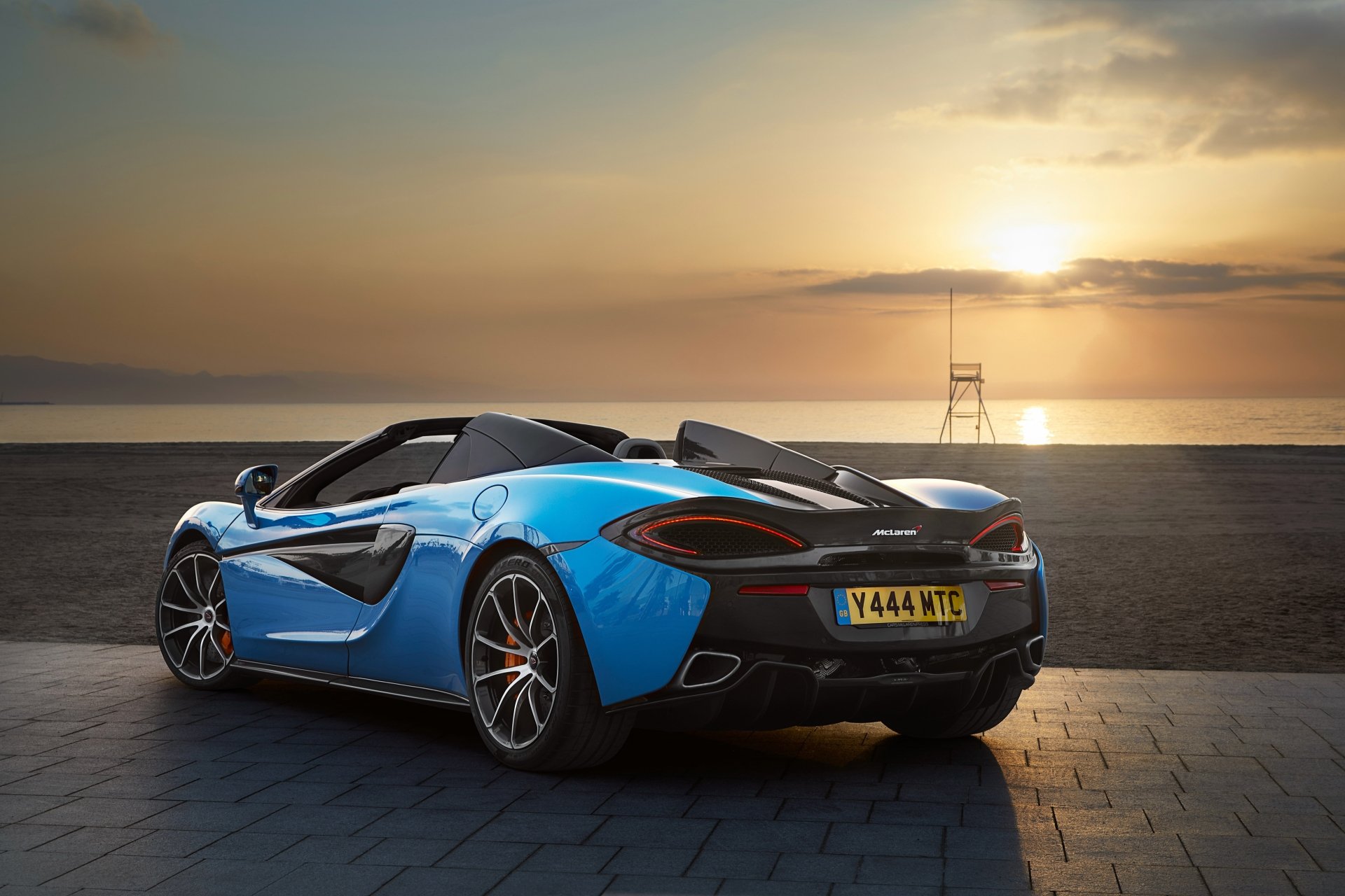 Blue McLaren 570S supercar parked on a coastal road at sunset, captured in 4K Ultra HD for a striking PC desktop wallpaper and background.
