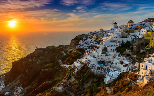 5K Ultra HD PC wallpaper: Santorini, Greece — man-made whitewashed town and windmills on a mountain cliff overlooking the sea and ocean at sunset with a golden horizon.