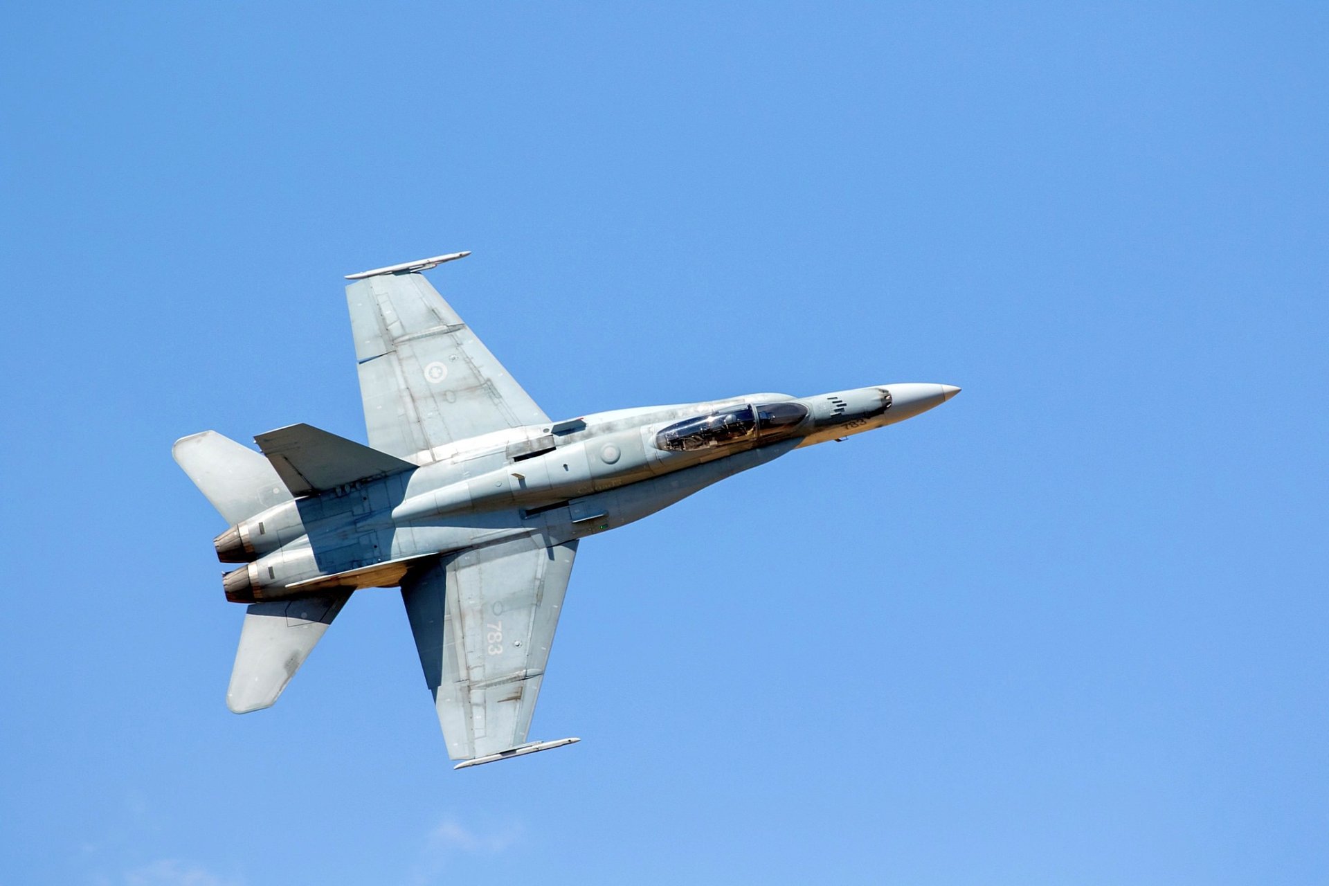 High-definition desktop wallpaper of a McDonnell Douglas CF-18 Hornet jet fighter soaring against a clear blue sky, showcasing its sleek military aircraft design.