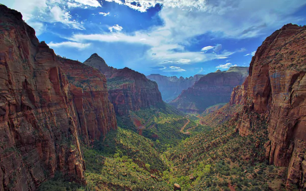 HD desktop wallpaper of a stunning forested canyon landscape at Zion National Park, with towering cliffs and a vibrant valley under a bright blue sky.