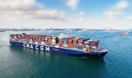 HD desktop wallpaper featuring the CMA CGM Antoine De Saint Exupery container ship carrying numerous colorful vehicles across calm waters.