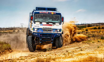 A Red Bull Kamaz rally truck speeds through sandy terrain, kicking up dust under a clear sky in this 4K Ultra HD sports vehicle wallpaper.
