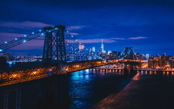 Night view of New York City featuring the illuminated Williamsburg Bridge over the water, captured in 4K Ultra HD as a vibrant cityscape background.