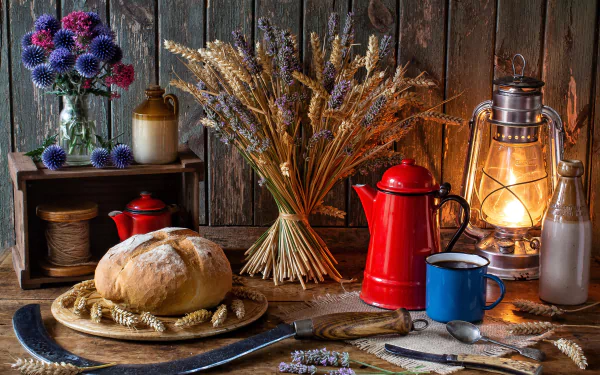 A serene still life HD desktop wallpaper featuring a loaf of bread, a red coffee pot, a blue mug, a lantern, and rustic elements like a bottle, spoon, knife, vase with flowers, and wheat stalks.
