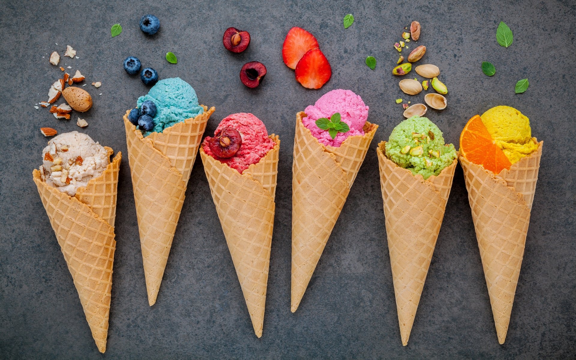 A vibrant 4K Ultra HD still life of six waffle cones filled with colorful ice cream scoops, garnished with fresh fruits, nuts, and herbs on a dark background.