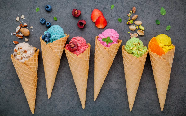 A vibrant 4K Ultra HD still life of six waffle cones filled with colorful ice cream scoops, garnished with fresh fruits, nuts, and herbs on a dark background.