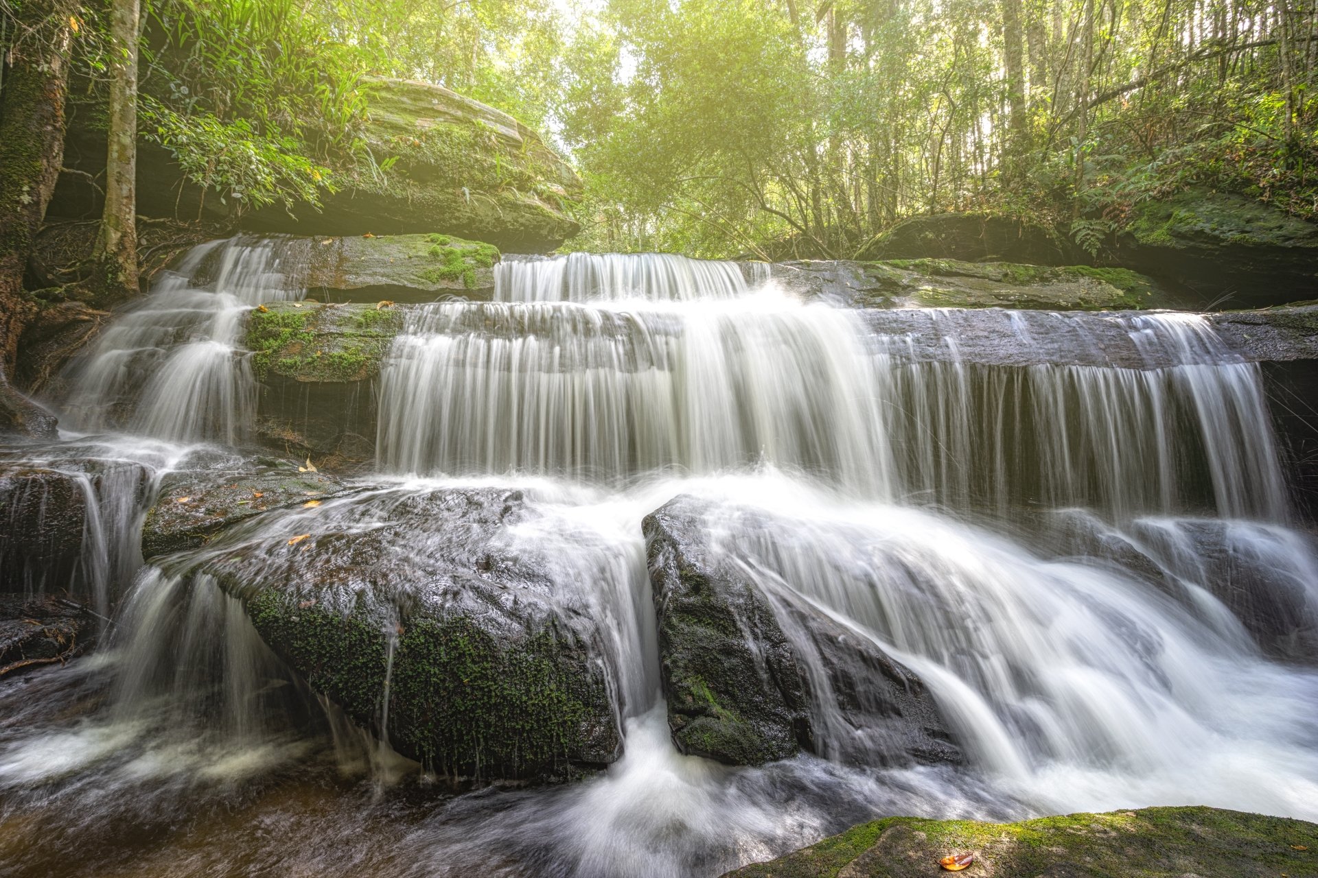 A serene multi-tiered waterfall cascading over moss-covered rocks in a lush forest, captured in stunning 4K Ultra HD for a nature-themed PC desktop wallpaper.