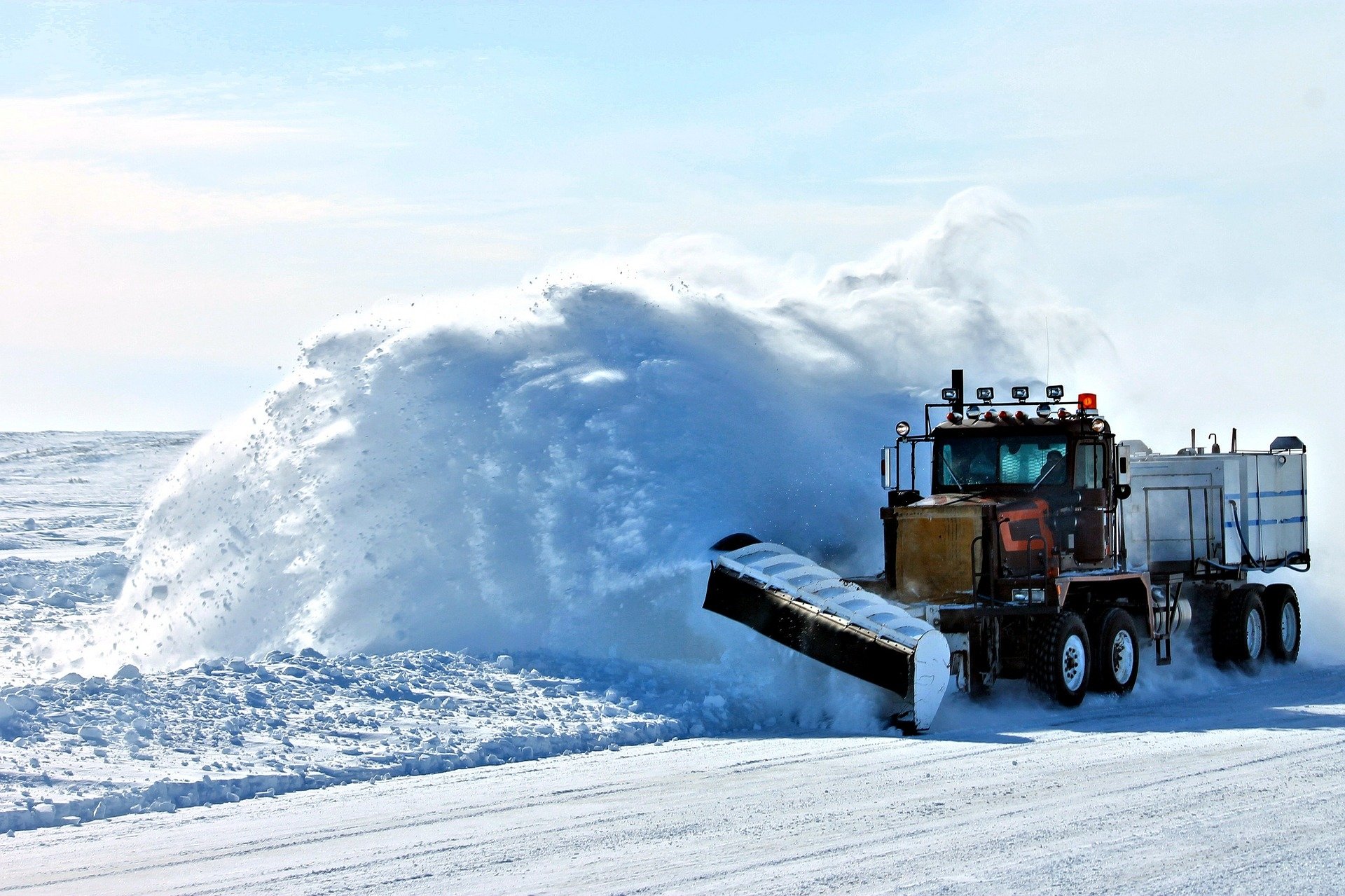 HD desktop wallpaper of a snowplow vehicle clearing deep snow on a bright winter day under a clear sky.
