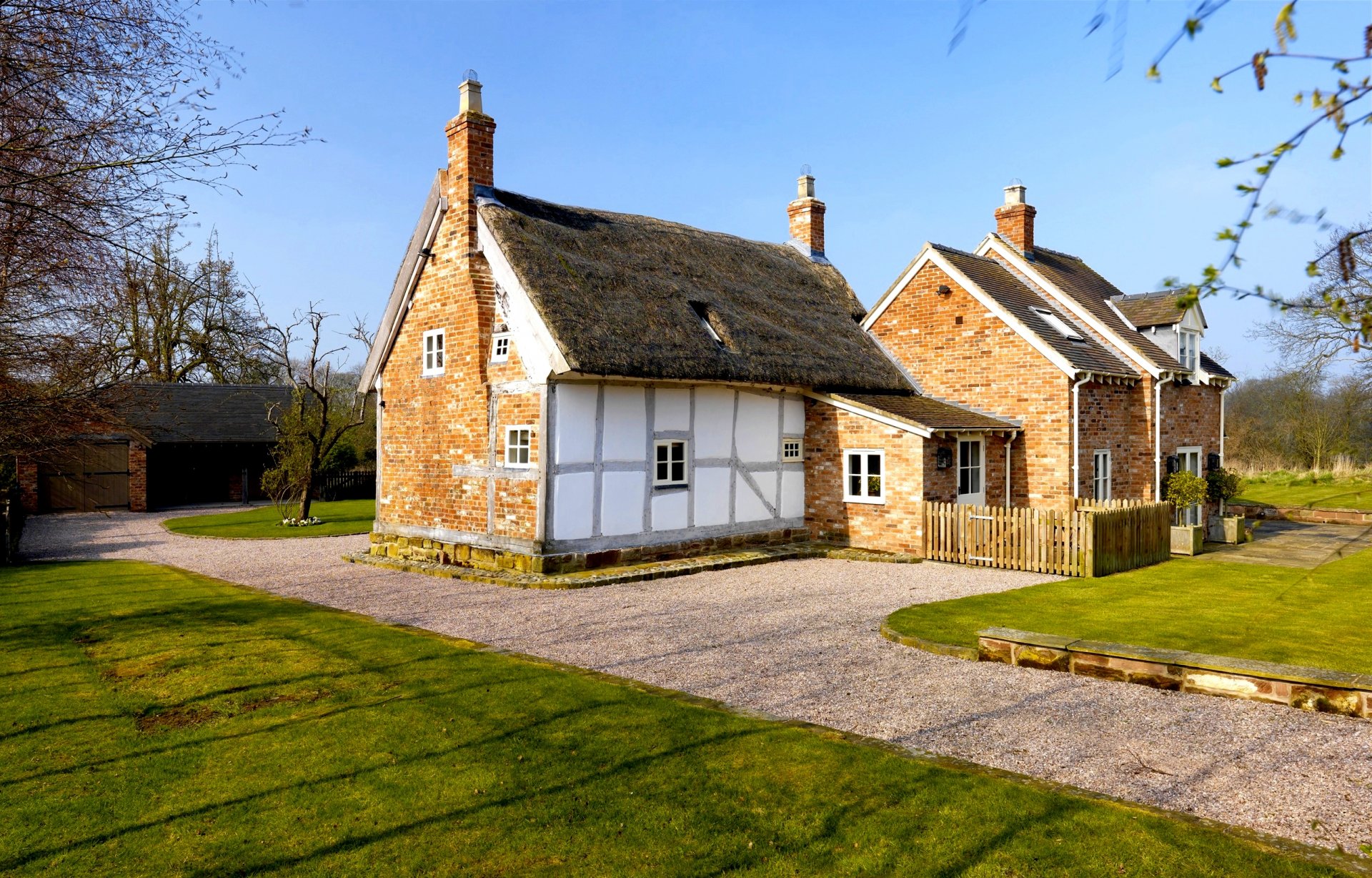 HD PC desktop wallpaper featuring a charming man-made brick and timber house set in a sunny, well-kept garden with clear blue skies.