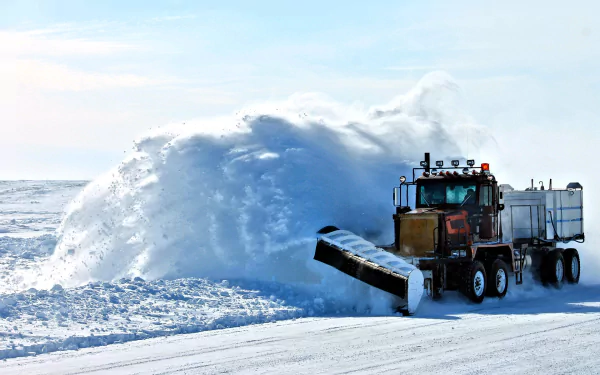 HD desktop wallpaper of a snowplow vehicle clearing deep snow on a bright winter day under a clear sky.