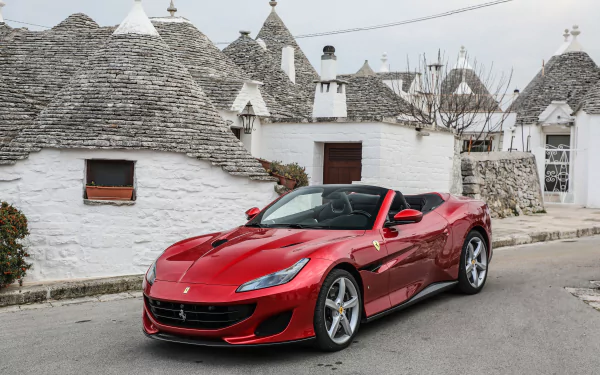 Red Ferrari Portofino supercar parked on a street with traditional white stone houses and conical roofs, captured in stunning 4K Ultra HD for PC desktop wallpaper.